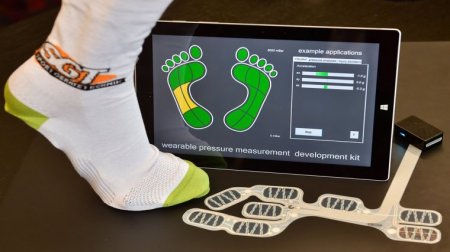 Ein Fuß mit Socke, davor eine Sensorleiste und ein Tablet, dass die Belastung des Fußes anzeigt. 