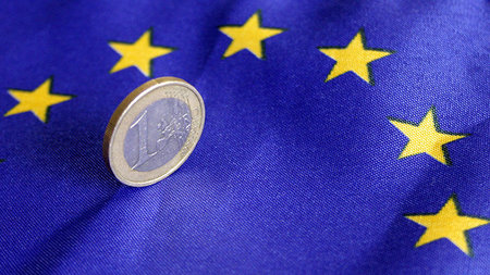 Eine 1-Euro-Münze steht auf einer Europaflagge