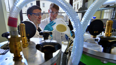 Zwei junge Forscher stehen vor einem Versuchsaufbau.