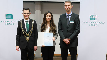 Asian woman stands between two men. She is holding a certificate.