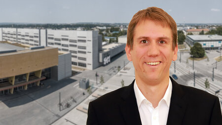 Mann im Anzug steht im Vordergrund, im Hintergrund sind Luftbild des Campus der TU Chemnitz Gebäude zu sehen.
