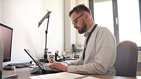 Eine junger Mann im Hemd mit Brille sitzt vor einen Computer.