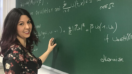 Eine Frau steht an einer Tafel, auf der Formeln stehen.
