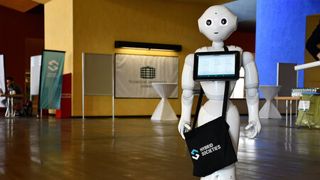 Ein Roboter hlt ein Tablet mit dem Logo des SFB Hybrid Societies.