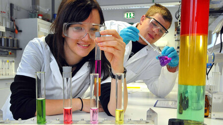 Ein Schüler und eine Schülerin experimentieren mit farbigen Substanzen in Reagenzgläsern im Labor.