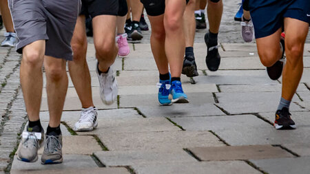 Bildausschnitt zeigt die Knie von nebeneinander laufenden Sportlern.