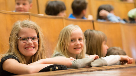 Zwei Mädchen sitzen in einem Hörsaal und lächeln.