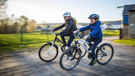 Zwei Kinder fahren nebeneinander auf dem Fahrrad.