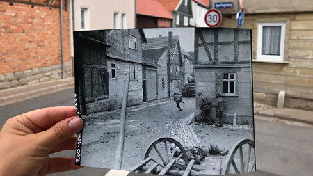 Ein Schwarz-Weiß-Foto, das einen auf einer Straße liegenden toten Soldaten zeigt, wird an einer Straßenecke hochgehalten. 
