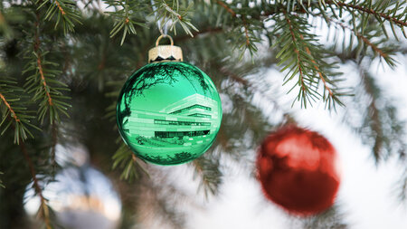 Weihnachtskugel, in der sich ein Gebäude spiegelt, hängt an einem Tannenzweig.
