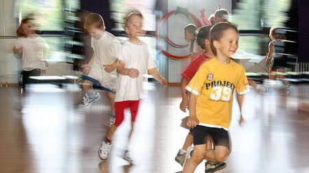 Mehrere Kinder rennen in einer Sporthalle.