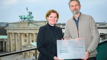 Eine FRau und ein Mann halten ein Schild in den Händen, im Hintergrund ist das Brandenburger Tor zu sehen.