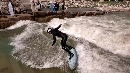 Ein Surfer steht auf einem Surfbrett in einem aufgewirbelten Fluss.