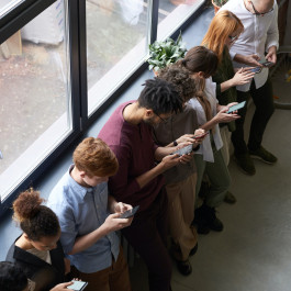 Mehrere Personen lehnen an einer Fensterbank und schauen auf ihre Smartphones.
