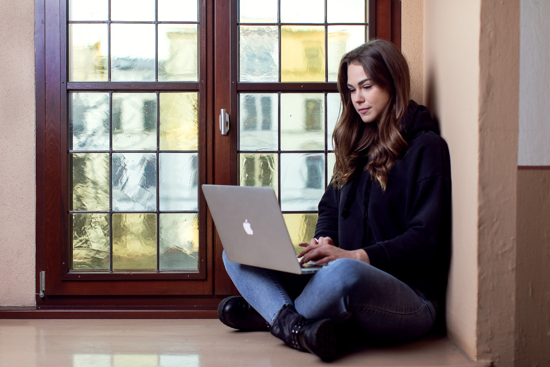junge Frau mit Notebook sitzt am Fenster