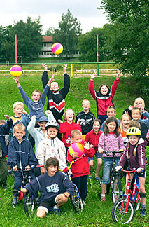 viele Kinder stehen zusammen auf Fahrrädern und werfen bunte Bälle in die Luft