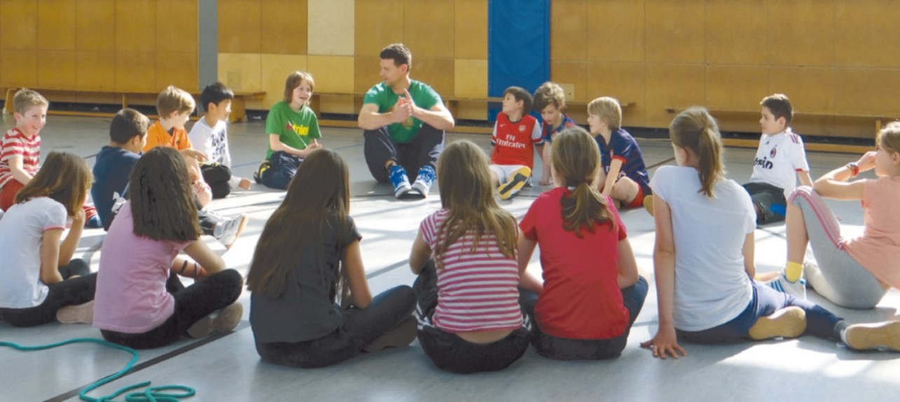 Bild einer Gruppe Kinder in einem Sitzkreis mit einem Betreuer