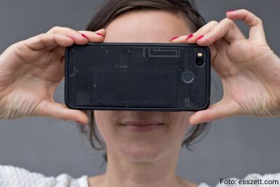 Photo of a smartphone user holding her smartphone in front of her face to remain anonymous