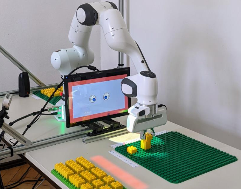 Robot-arm setup including display with eyes constructing something with lego duplo like bricks.