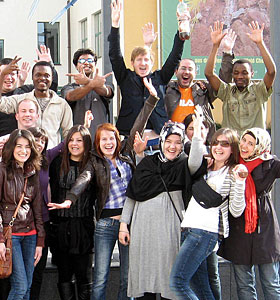 Bild mit eine Ausschnitt einer Gruppe internationaler Studierende, die die Hände in Luft reißen und sich freuen.
