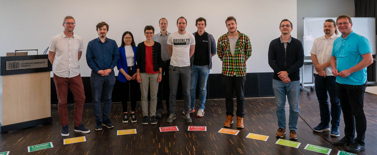 9 stramme Männer und 2 Frauen posieren für ein Gruppenfoto vor einer Glaswand