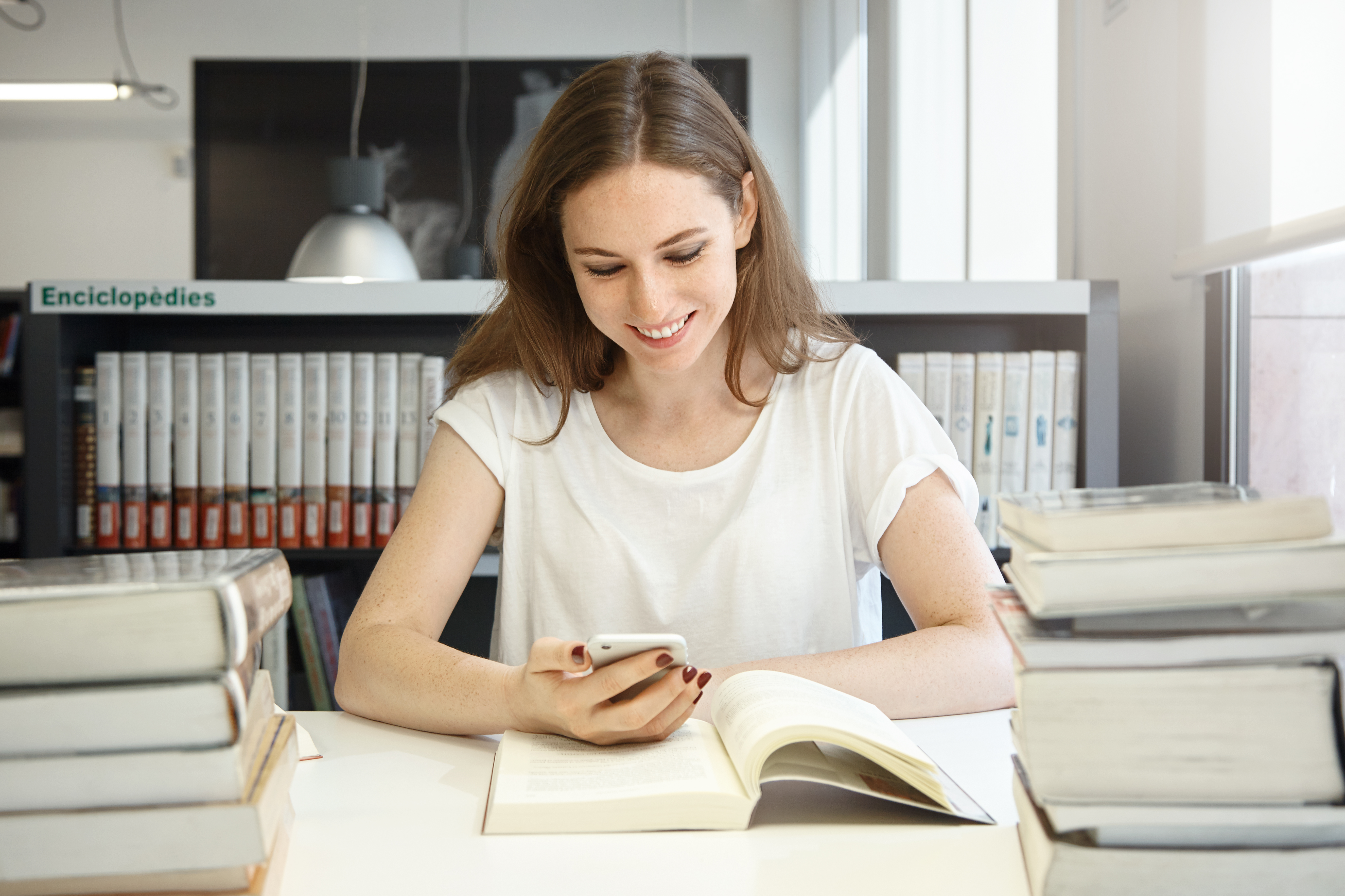 Image of a young woman at a library looking down at her smartphone