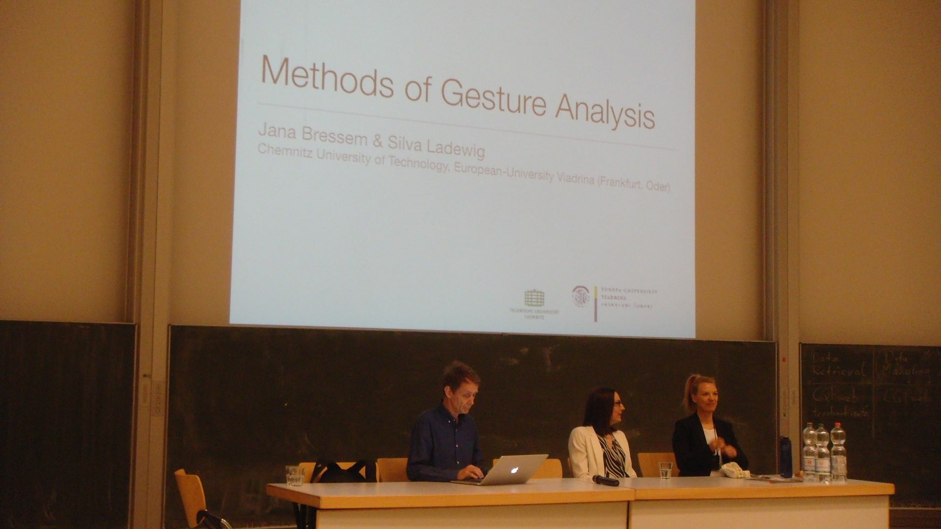 2 Sprecher und 1 Sprecherin sitzen am Podium, im Hintergrund Deckblatt der Präsentation "Methods of Gesture Analysis"