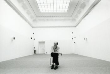 Ein Mann sitzt auf einem Stuhl in einem leeren Ausstellungsraum mit mehreren Lautsprechern