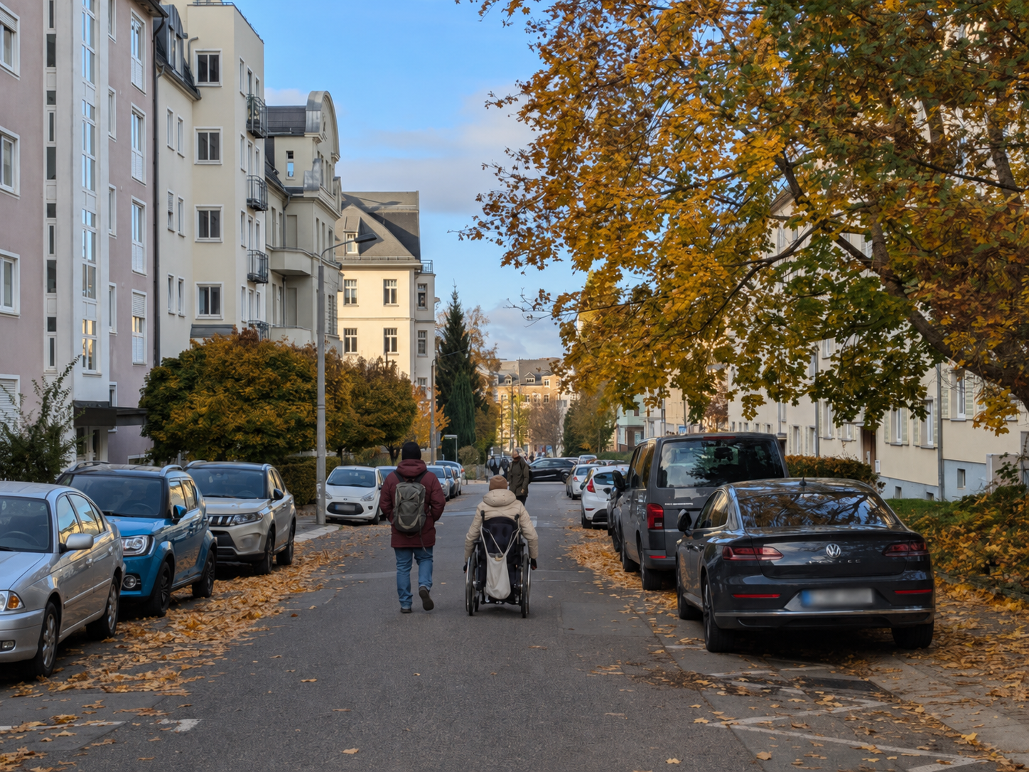 Eine ältere Person mit Rollator geht auf der Fahrbahn einer sonnigen Wohnstraße. Rechts und links stehen parkende Autos; die Gehwege sind teilweise schmal oder durch Fahrzeuge und andere Hindernisse schwer zugänglich. Im Hintergrund sind mehrstöckige Wohnhäuser und Bäume zu sehen.