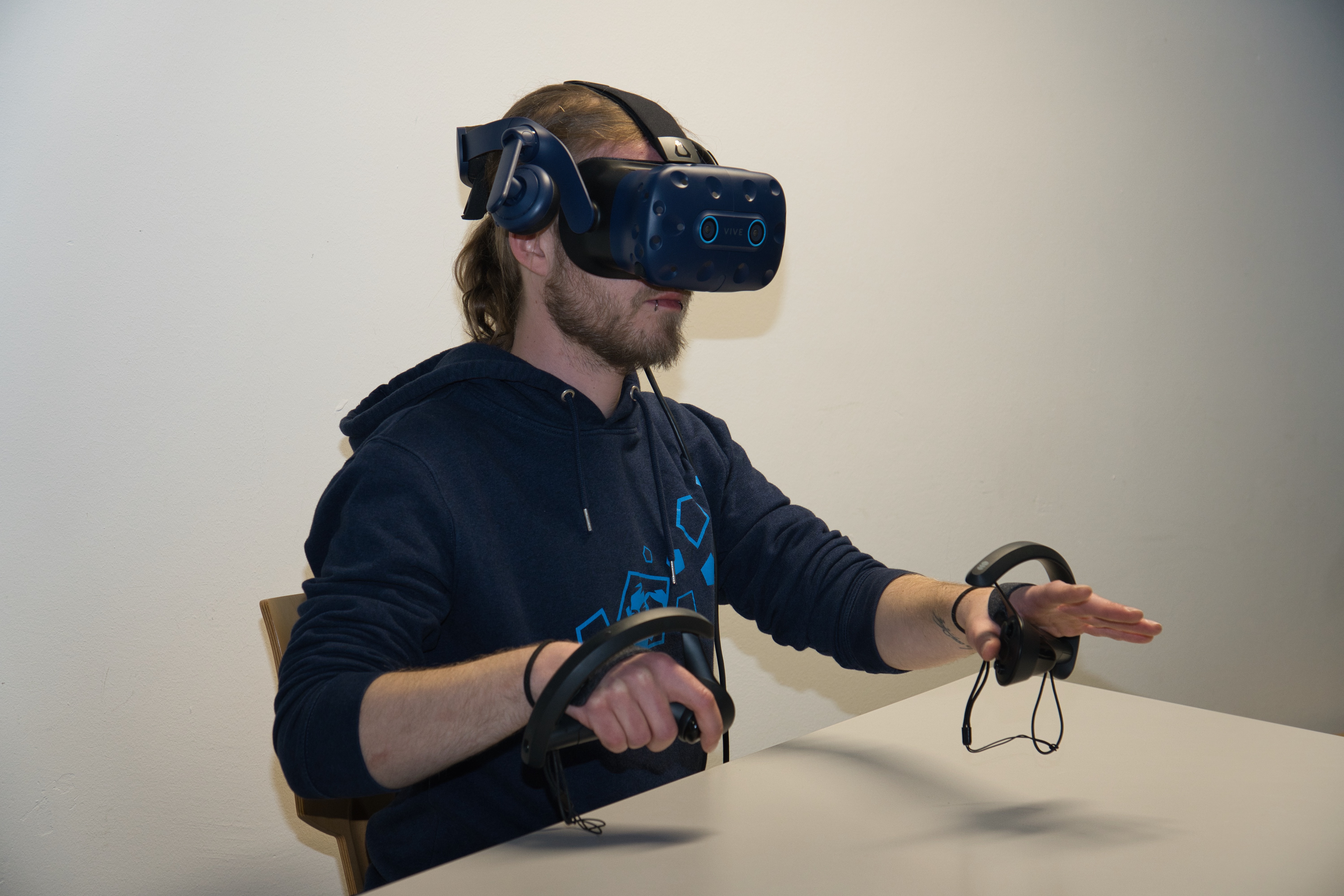 Person mit VR-Brille und Controller sitzt an einem Tisch.