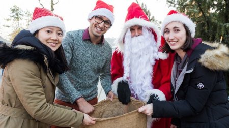 Der Weihnachtsmann und drei Studierende laden lachend zum TU-Weihnachtsmarkt ein.