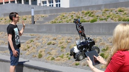 Roboter auf vier Rädern blickt mit Kamera auf eine männliche Person.