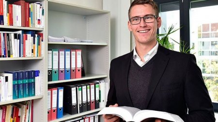 Junger Mann mit Brille hält ein Buch.