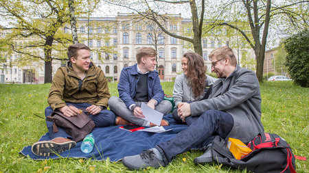 Vier Schüler sitzen auf einer Decke im Park gegenüber dem TU-Hauptgebäude.