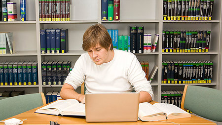 Junger Mann sitzt am Tisch und arbeitet am Laptop