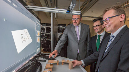 Drei Männer, unter ihnen TU-Rektor Gerd Strohmeier, stehen vor einem Computer