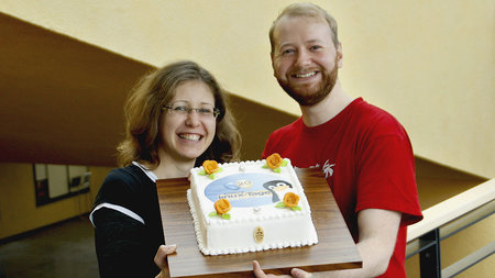 Ein Mann und eine Frau halten eine Geburtstagstorte in die Kamera