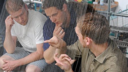 Drei Männer sitzen, während zwei nachdenklich schauen und einer mit ihnen redet.