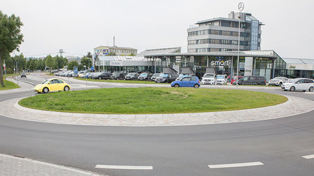 Keisverkehr, auf welchem zwei Autos fahren und ein drittes den Kreisverkehr soeben erreicht