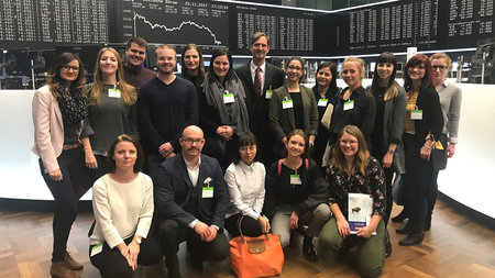 Gruppenfoto mehrerer Personen in der Frankfurter Börse mit riesigen Monitoren im Hintergrund