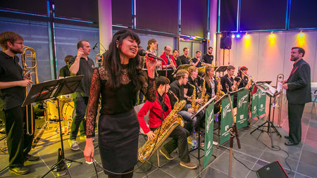 Eine Band hält ein Konzert, bei dem eine Frau im Vordergrund singt