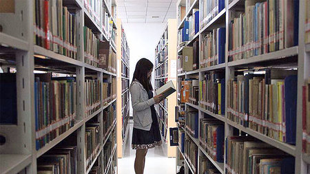 Asiatische Studentin steht vor einem Bücherregal.