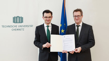 Prof. Dr. Gerd Strohmeier und Prof. Dr. Stefan Garsztecki halten Stellenausschreibung in der Hand