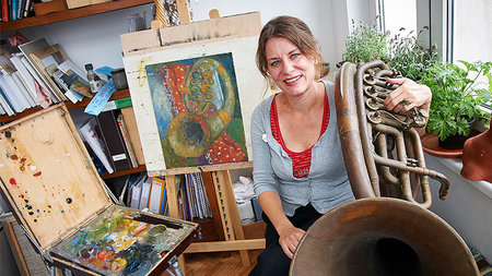 Frau sitzt umgeben von Gemälden.