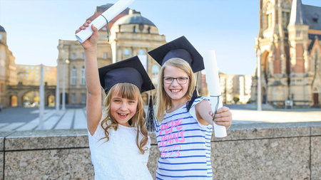 Zwei Schülerinnen halten Diplome hoch.