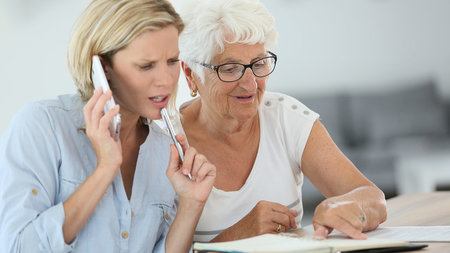 Junge Frau, die Handy ans Ohr hält und Stift in der Hand hat, berät Seniorin.