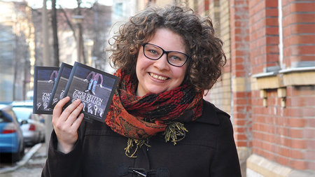 Junge Frau lächelt und hält drei CDs ihres ersten Hörbuchs in der rechten Hand.