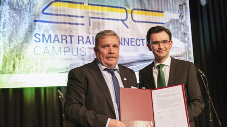 Oberbürgermeister Rolf Schmidt und Rektor Gerd Stohmeier halten den unterzeichneten Vertrag hoch.