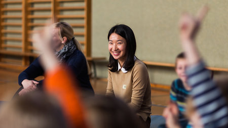 Jun.-Prof. Dr. Minkyung Kim sitzt in einer Turnhalle und spricht mit Schülern.