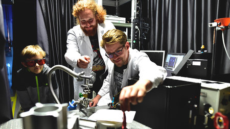 Zwei Wissenschaftler erläutern einem Jungen den Versuchsaufbau in einem Laserlabor der Physiker.